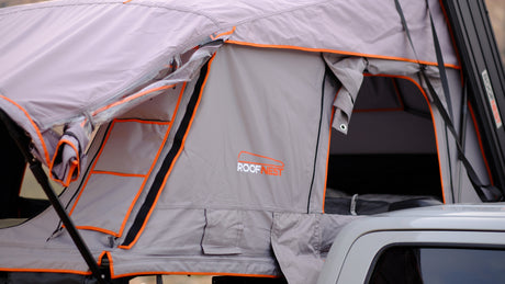 Open gray and orange Roofnest rooftop tent on a white vehicle, ideal for your next RV rental camping trip.