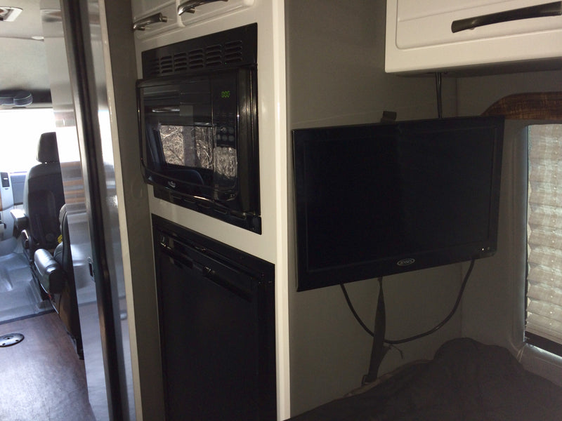 RV rental interior: Built-in microwave, fridge, and TV setup next to a sleeping area. Compact and functional space. — photo 5