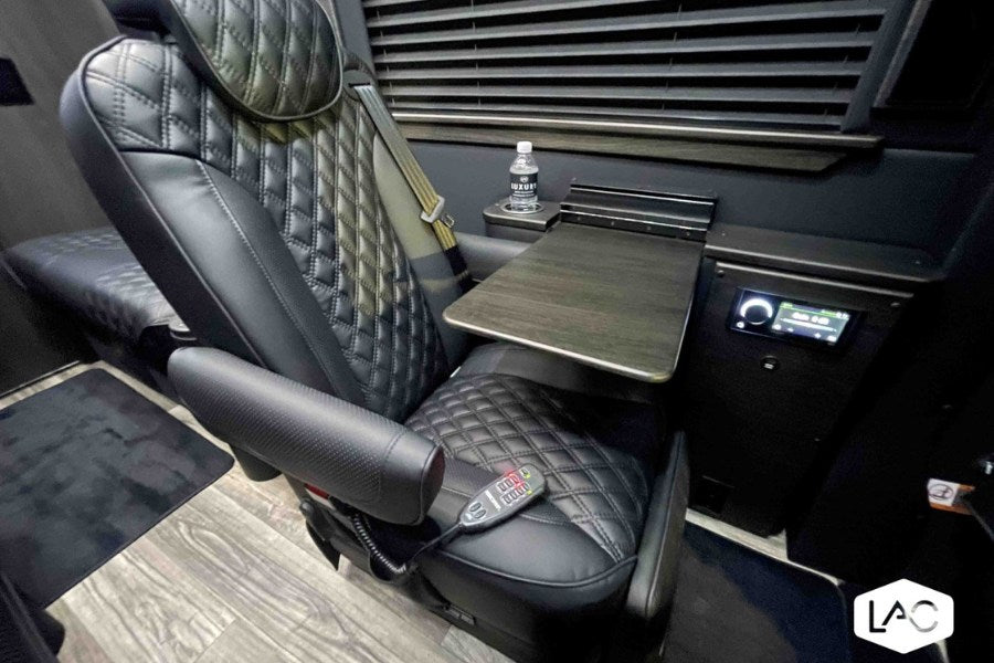  featuring plush black leather captain's chairs & tech screen.|Luxury custom van interior for rv rental: two black quilted leather captain's chairs — photo 3