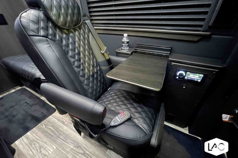  featuring plush black leather captain's chairs & tech screen.|Luxury custom van interior for rv rental: two black quilted leather captain's chairs — photo 3