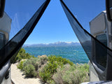 Stunning lake view from an RV rental, framed by screens. Snowy mountains across sparkling water and green plants.