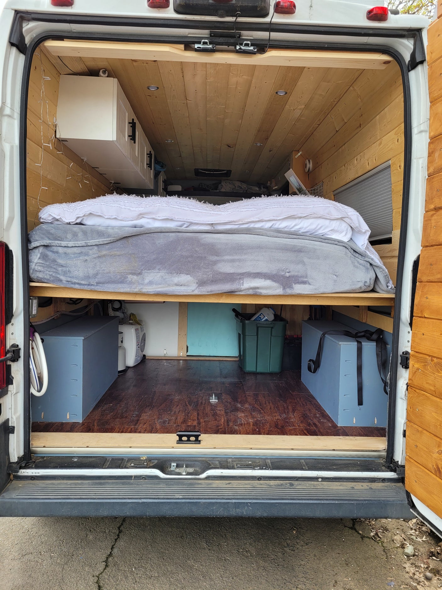 Spacious RV rental interior with a cozy bed, wood paneling, and ample storage under the bed. Perfect for van life adventures.