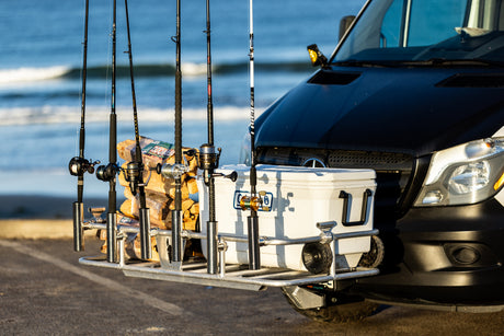 An RV rental van equipped for a beach fishing trip, with rods, cooler, and firewood on its front carrier.