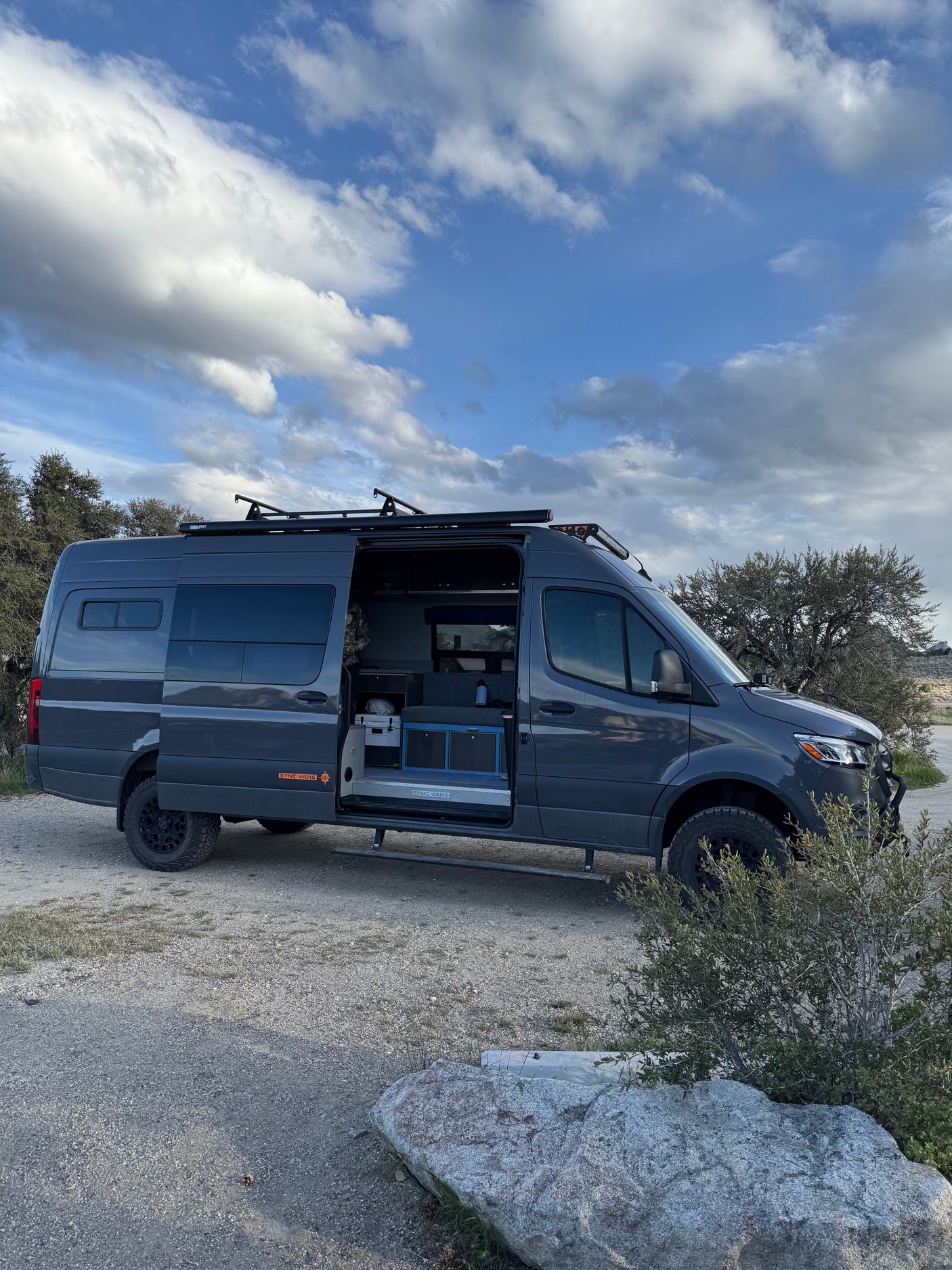 Adventure-ready custom Mercedes Sprinter camper van for rv rental, parked outdoors. Open door shows interior.