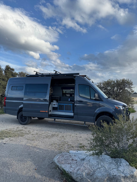 Adventure-ready custom Mercedes Sprinter camper van for rv rental, parked outdoors. Open door shows interior.
