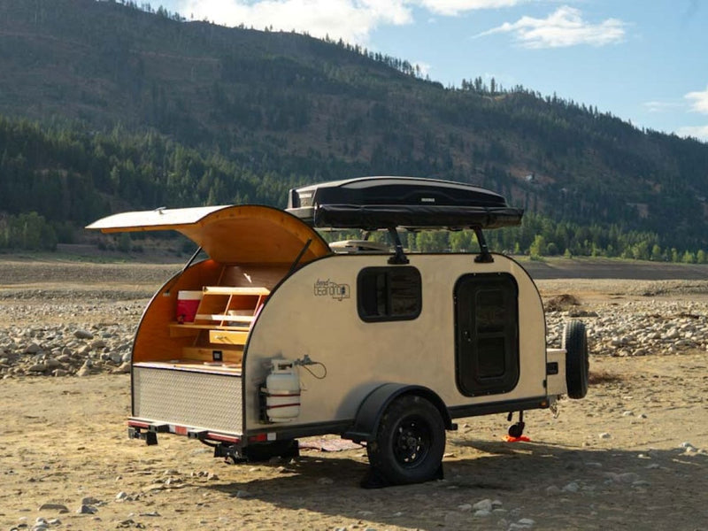This RV rental teardrop trailer with an open galley sits on a rocky shore — photo 1