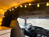 Cozy RV rental interior showcasing custom wood ceiling, warm string lights, and a view into the driver's cabin.