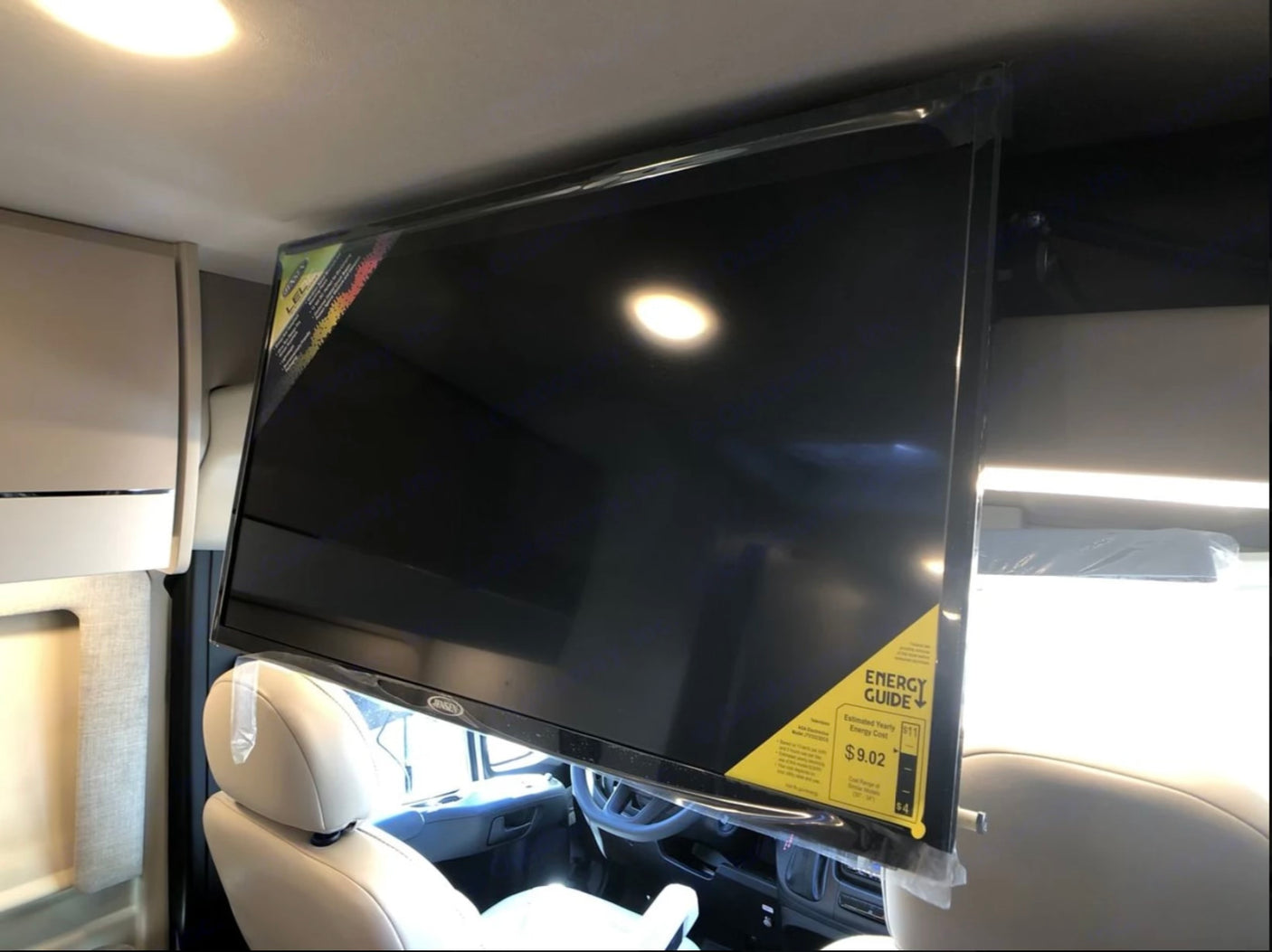 View inside an RV rental showing a new, ceiling-mounted JENSEN TV with its Energy Guide sticker, overlooking the front cabin.