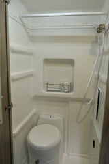 Inside an RV rental: a compact, all-in-one wet bath featuring a toilet, shower, and small storage shelf.