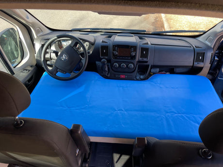 Inside an RV rental van: The front cab, including dashboard & steering wheel, converted to a sleeping area with a bright blue mattress.