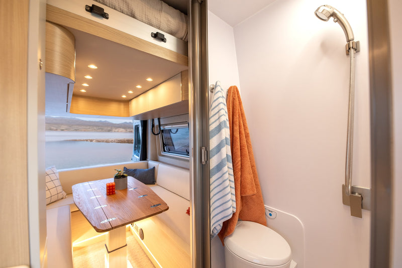 Modern rv rental interior showing a dining area with scenic lake views, opposite a compact bathroom with a toilet and shower. — photo 5