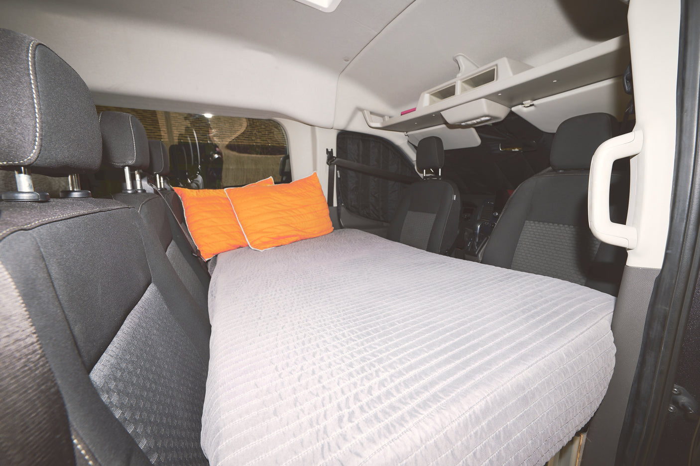 Inside this RV rental, a grey mattress and orange pillows are arranged as a bed, perfect for vehicle camping.