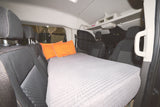 Inside this RV rental, a grey mattress and orange pillows are arranged as a bed, perfect for vehicle camping.