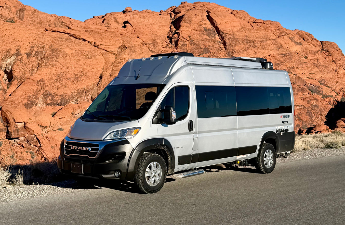 Silver Ram ProMaster camper van RV rental parked against striking red rock landscapes, ready for desert adventures.