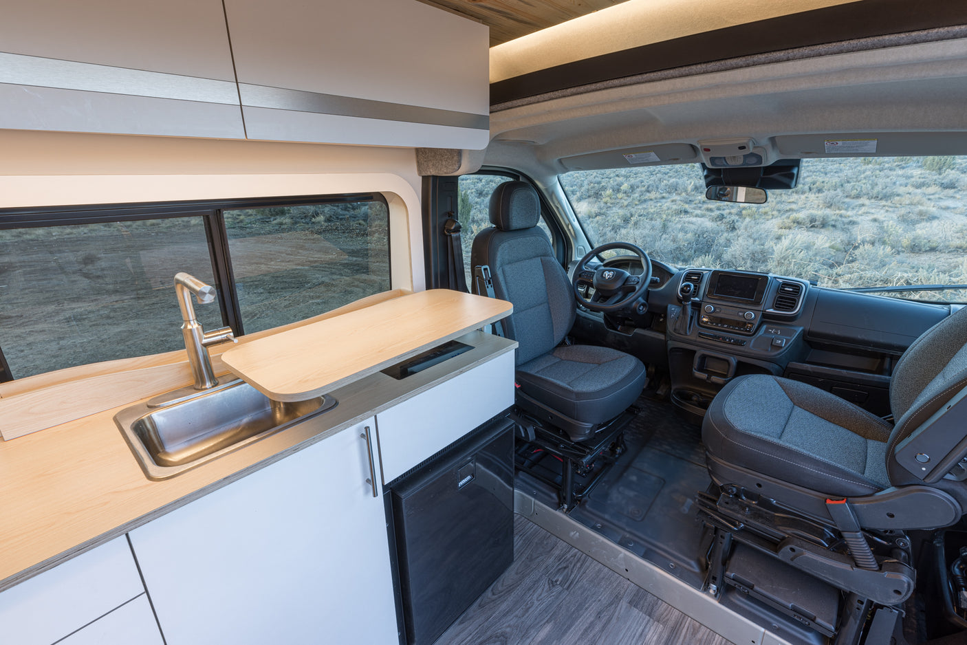 Modern RV rental interior: kitchen with sink, wood counters, fridge, and spacious front cabin.