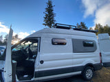 White rv rental camper van with open driver's door, custom side windows, and roof rack, ready for adventure.