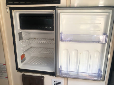 An open, empty refrigerator and freezer inside an RV rental, ready for your next adventure.