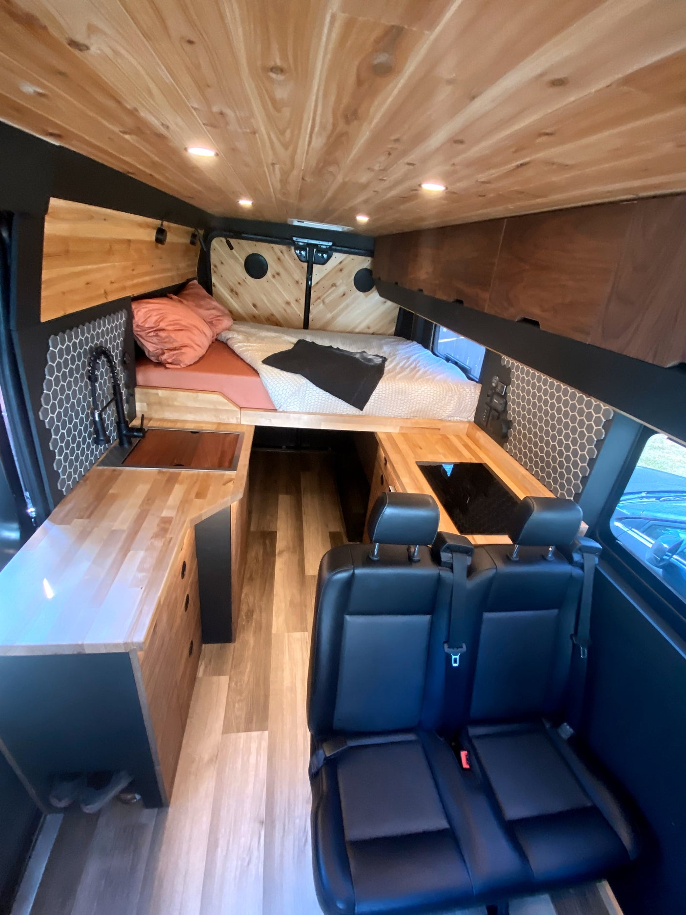 Stylish RV rental: wood-paneled ceiling, hexagon tiles, comfy bed, kitchenette, and passenger seating for adventure.