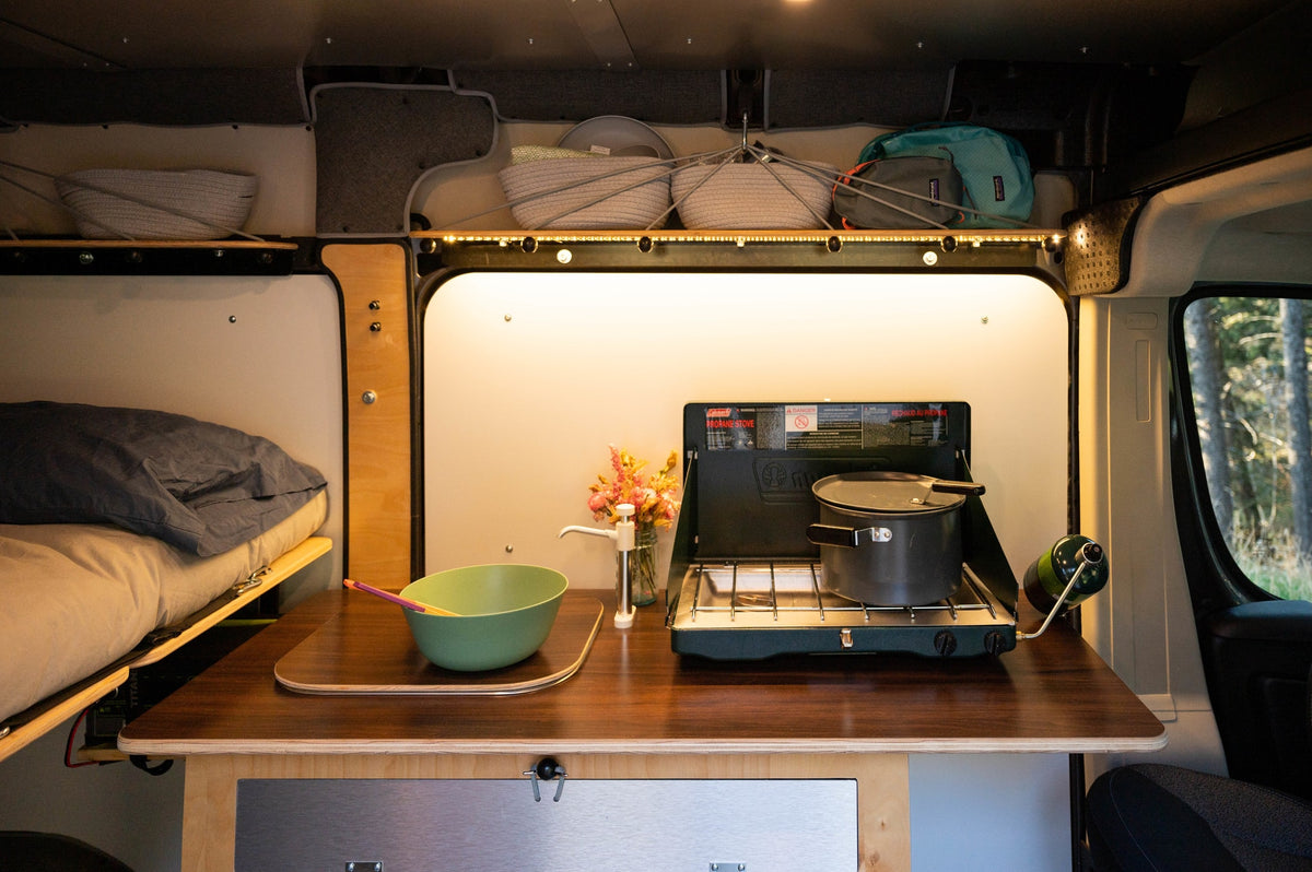 RV rental: Campervan interior featuring kitchen with propane stove & pot, bed, storage, and sink pump for travel. — photo 14