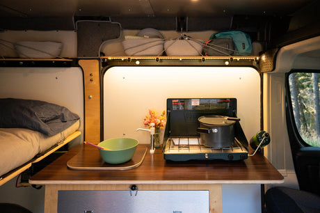 RV rental: Campervan interior featuring kitchen with propane stove & pot, bed, storage, and sink pump for travel.