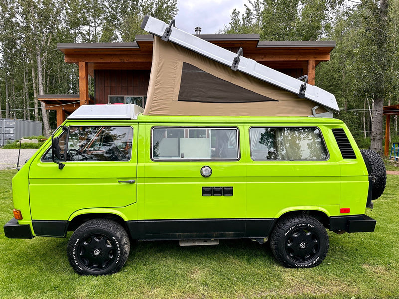  this van life scene shows a woman relaxing inside.|Green pop-top VW van parked in a grassy field with a picnic table — photo 5