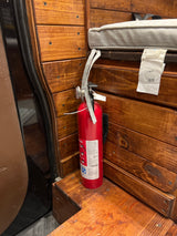 Essential safety gear: a red fire extinguisher secured to the wooden interior of an RV rental, with a grey cushion nearby.