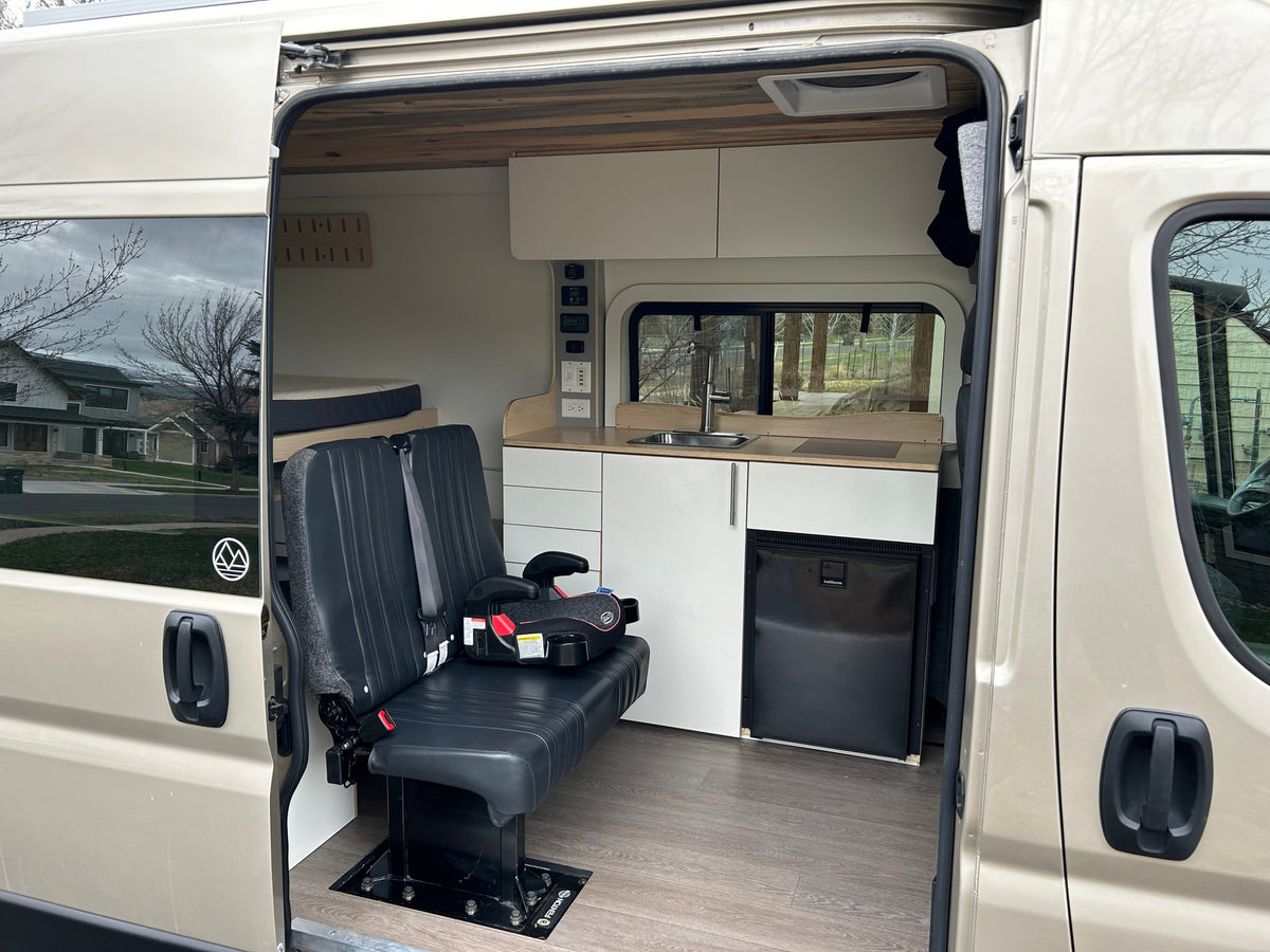 Spacious RV rental camper van interior featuring custom kitchen, bench seating with child booster, and rear bed. — photo 2