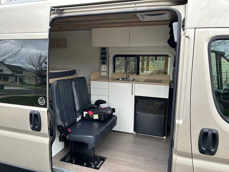 Spacious RV rental camper van interior featuring custom kitchen, bench seating with child booster, and rear bed. — photo 2