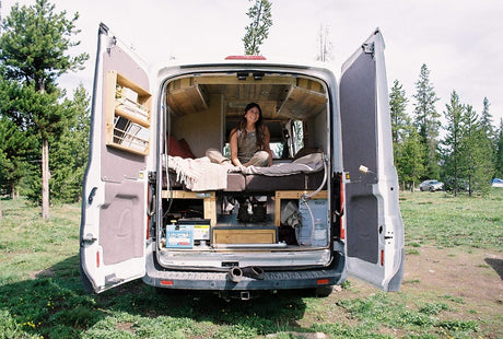 Smiling woman in her custom camper van, set up for adventure. An ideal RV rental for exploring nature and van life travel.