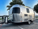 Sleek silver Airstream travel trailer, hitched up for an RV rental adventure. Parked on asphalt under a clear blue sky.
