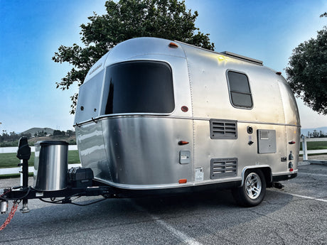 Sleek silver Airstream travel trailer, hitched up for an RV rental adventure. Parked on asphalt under a clear blue sky.