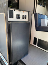 RV rental interior showing a compact refrigerator, control panel with switches, and blue/white seating.