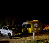 Night camping scene with an Airstream RV rental, silver truck, and tent under starry skies.