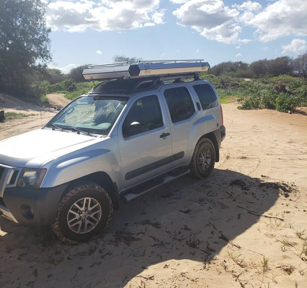 Silver Nissan Xterra SUV with a rooftop tent on a sandy road, ready for adventure camping. Explore with this RV rental alternative.