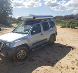 Silver Nissan Xterra SUV with a rooftop tent on a sandy road, ready for adventure camping. Explore with this RV rental alternative.