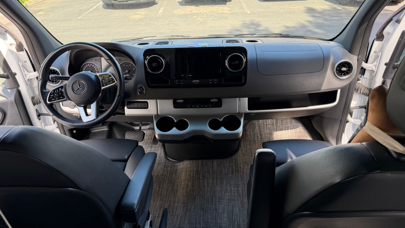 RV rental's front cabin: A modern Mercedes-Benz Sprinter dashboard with steering wheel, infotainment screen, and front seats.