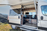 This rv rental reveals its spacious interior with an open door, extended awning, and cozy seating area overlooking mountains.