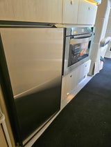 RV rental kitchen: stainless Contoure microwave & fridge, secured with a 'MOVING ON UP' latch, within light wood cabinetry.