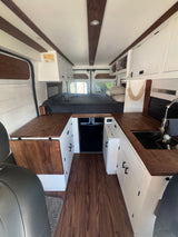 RV rental: Bright, modern camper van interior with a bed, kitchen sink, and wooden accents throughout.