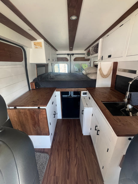 RV rental: Bright, modern camper van interior with a bed, kitchen sink, and wooden accents throughout.