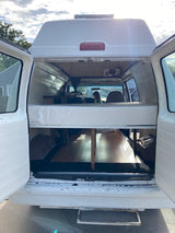 RV rental camper van interior. Features a convertible bed/bench, built-in storage, and visible front cab, ready for travel.