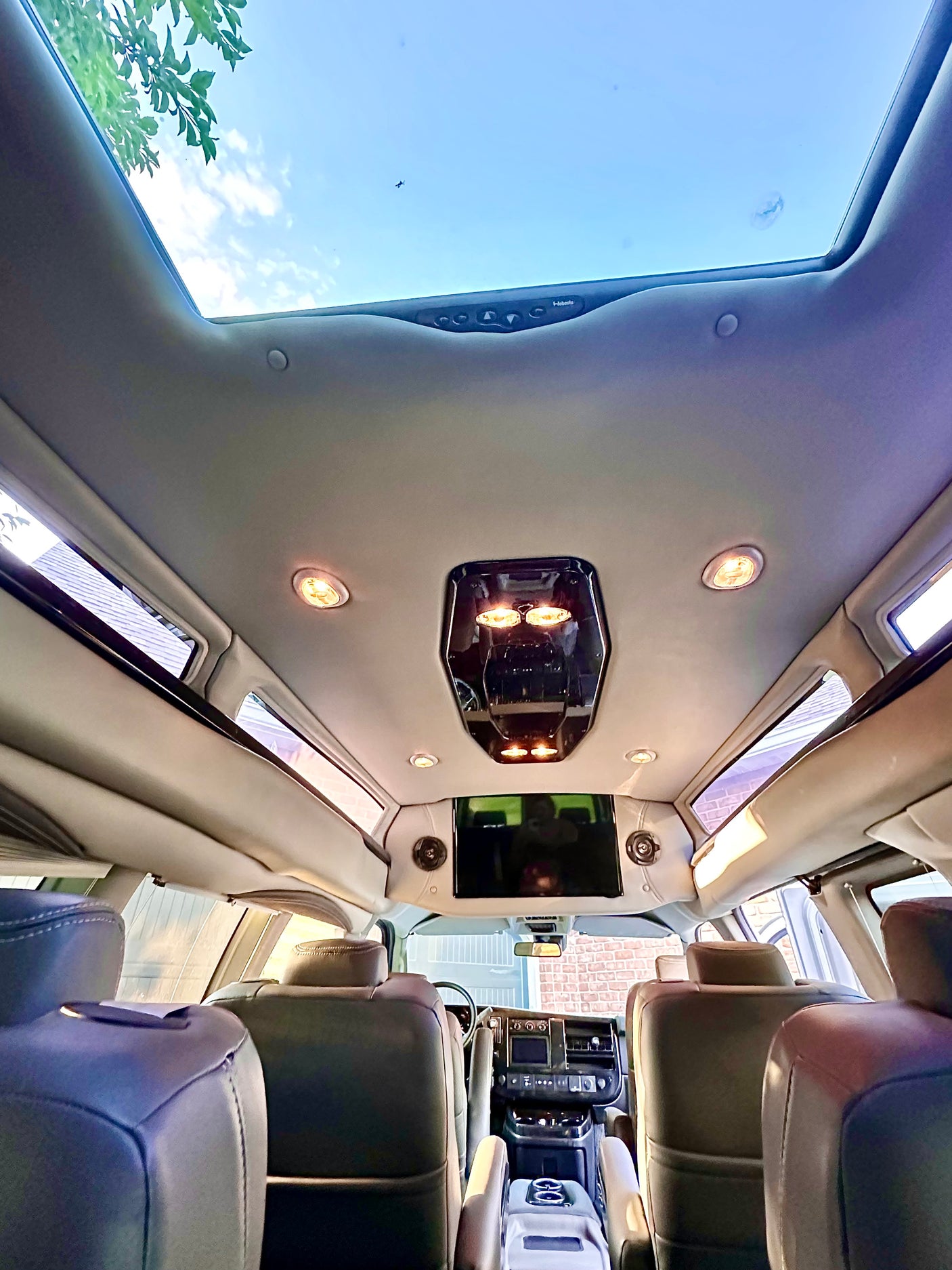 Inside a luxurious RV rental conversion van, featuring plush seats, a large skylight, and a mounted screen.