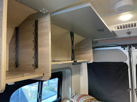 RV rental: open overhead storage cabinets reveal a functional camper interior with a window, ceiling light, and AC vent.