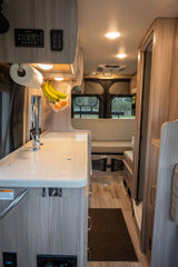 RV rental interior: Light wood kitchen counter, sink, overhead controls, and cozy seating in a compact camper.