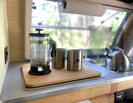 Cozy RV rental kitchen featuring a French press, mugs, and kettle. Ideal for brewing coffee on camping trips.