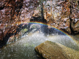 Vibrant rainbow arcs through waterfall spray over dark rocks & water. Enjoy natural beauty with an RV rental.