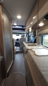 Bright RV rental interior: modern kitchen with sink, overhead lights, and sleek storage extending towards the front cabin.