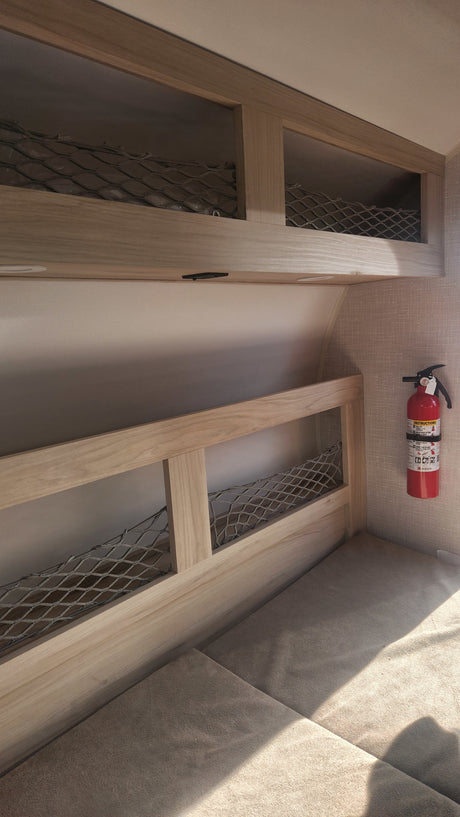 RV rental interior: light wood storage with netting, a padded area, and a red fire extinguisher mounted on a textured wall.