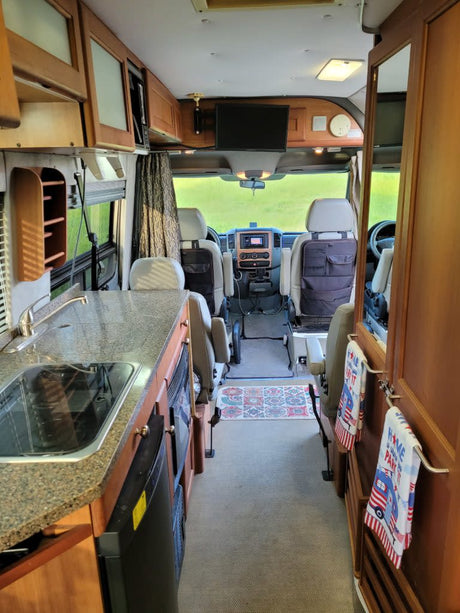 Explore this RV rental's cozy interior: compact kitchen, captain's chairs, front cockpit, and overhead storage.