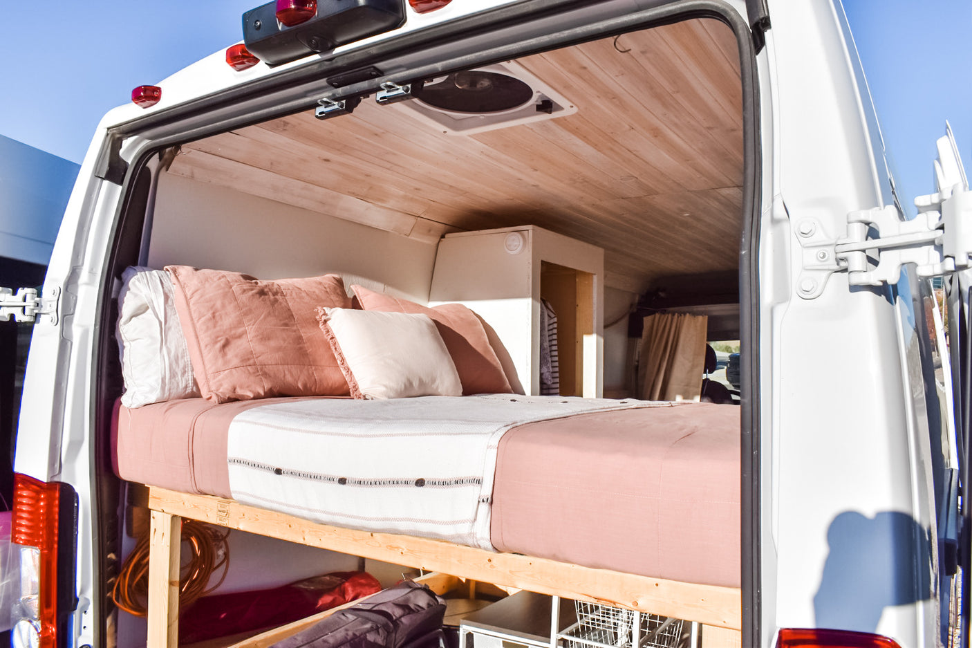 Discover this RV rental's cozy interior, featuring a bed with blush linens, wood ceiling, and clever under-bed storage.